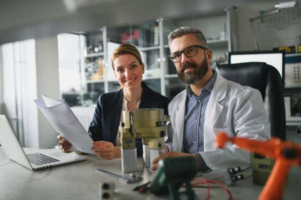 Robotics engineers working on a laptop and desinging modern robotic arm in laboratory.