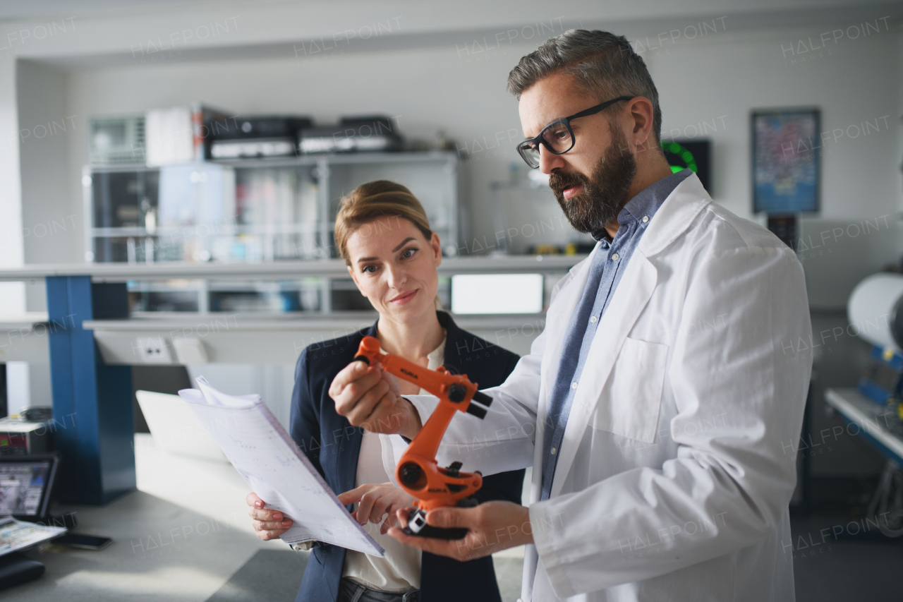 Robotics engineers with blueprints dicussing and desinging a modern robotic arm in laboratory.