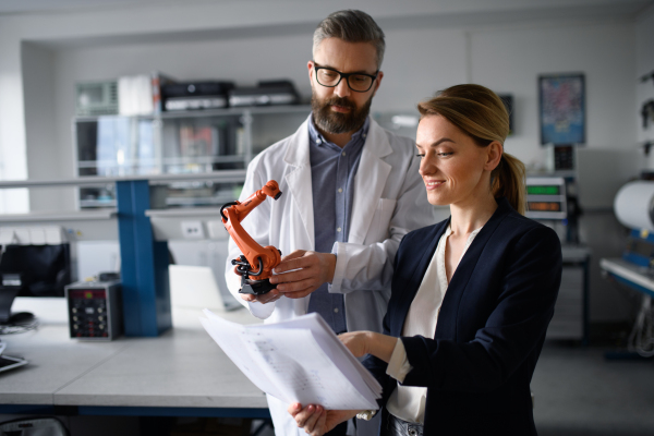 Robotics engineers with blueprints dicussing and desinging a modern robotic arm in laboratory.