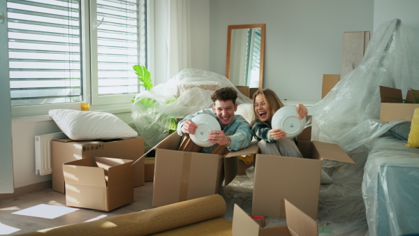 A cheerful young couple in their new apartment, having fun when unpacking. Conception of moving.