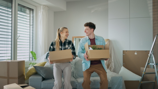 A cheerful young couple in their new apartment, carrying boxes. Conception of moving.