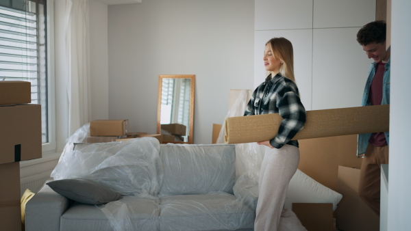 A cheerful young couple in their new apartment, carrying carpet. Conception of moving.