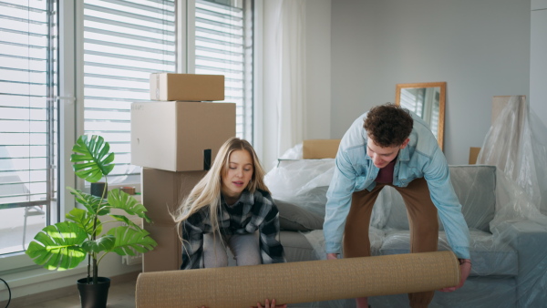 A cheerful young couple in their new apartment, rolling out carpet. Conception of moving.