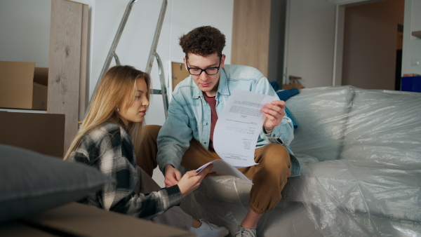 A cheerful young couple in their new apartment, sitting on floor and reading papers. Conception of moving.