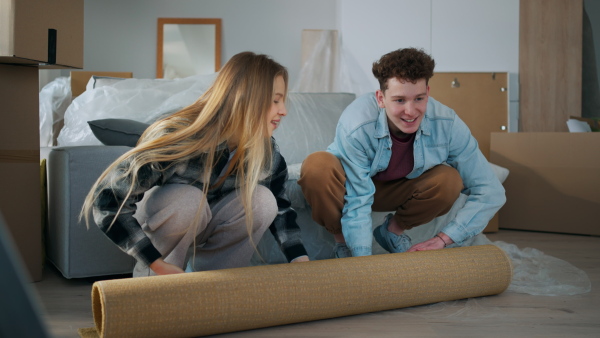 A cheerful young couple in their new apartment, rolling out carpet. Conception of moving.