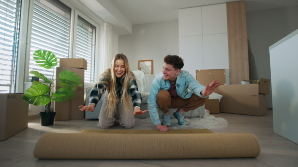 A cheerful young couple in their new apartment, rolling out carpet. Conception of moving.