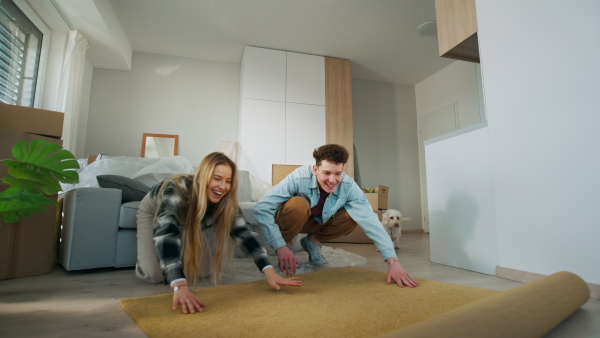 A cheerful young couple in their new apartment, rolling out carpet. Conception of moving.