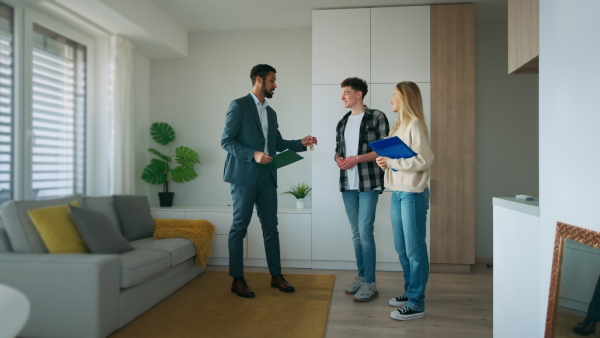 A happy young couple buying their new home and meeting real estate agent in apartment.