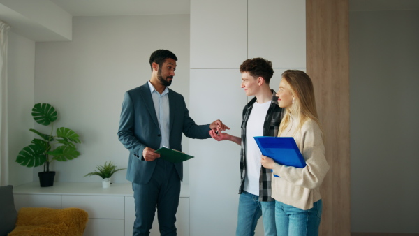 A happy young couple buying their new home and meeting real estate agent in apartment.