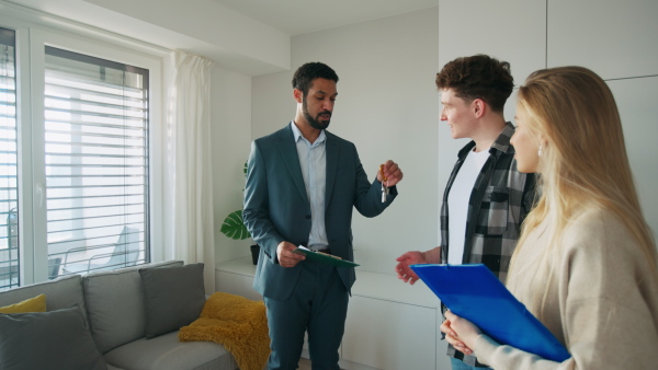 A happy young couple buying their new home and meeting real estate agent in apartment.