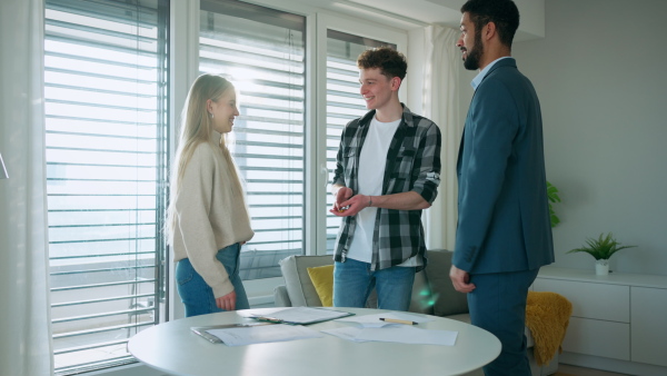 A young couple signing contract when buying their new home and receiving keys from real estate agent.