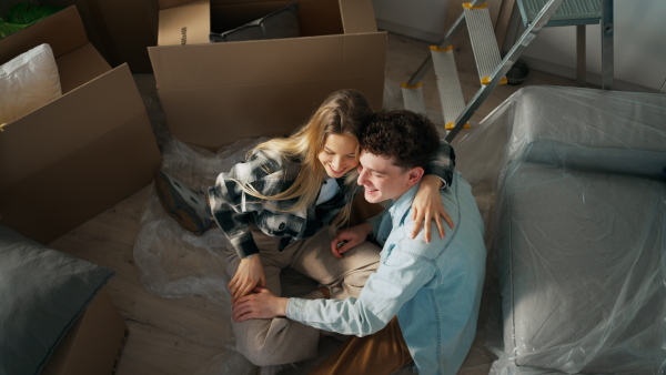 A cheerful young couple in their new apartment, sitting on floor and hugging. Conception of moving.