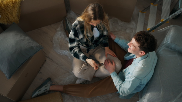 A cheerful young couple in their new apartment, sitting on floor and hugging. Conception of moving.