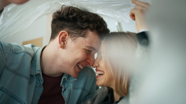 A cheerful young couple in love in their new apartment, sitting on floor and and laughing. Conception of moving.