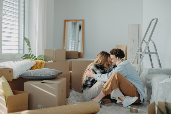 A cheerful young couple in their new apartment, sitting on floor and hugging. Conception of moving.