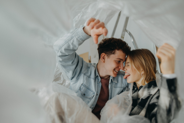 A cheerful young couple in love in their new apartment, sitting on floor and and laughing. Conception of moving.