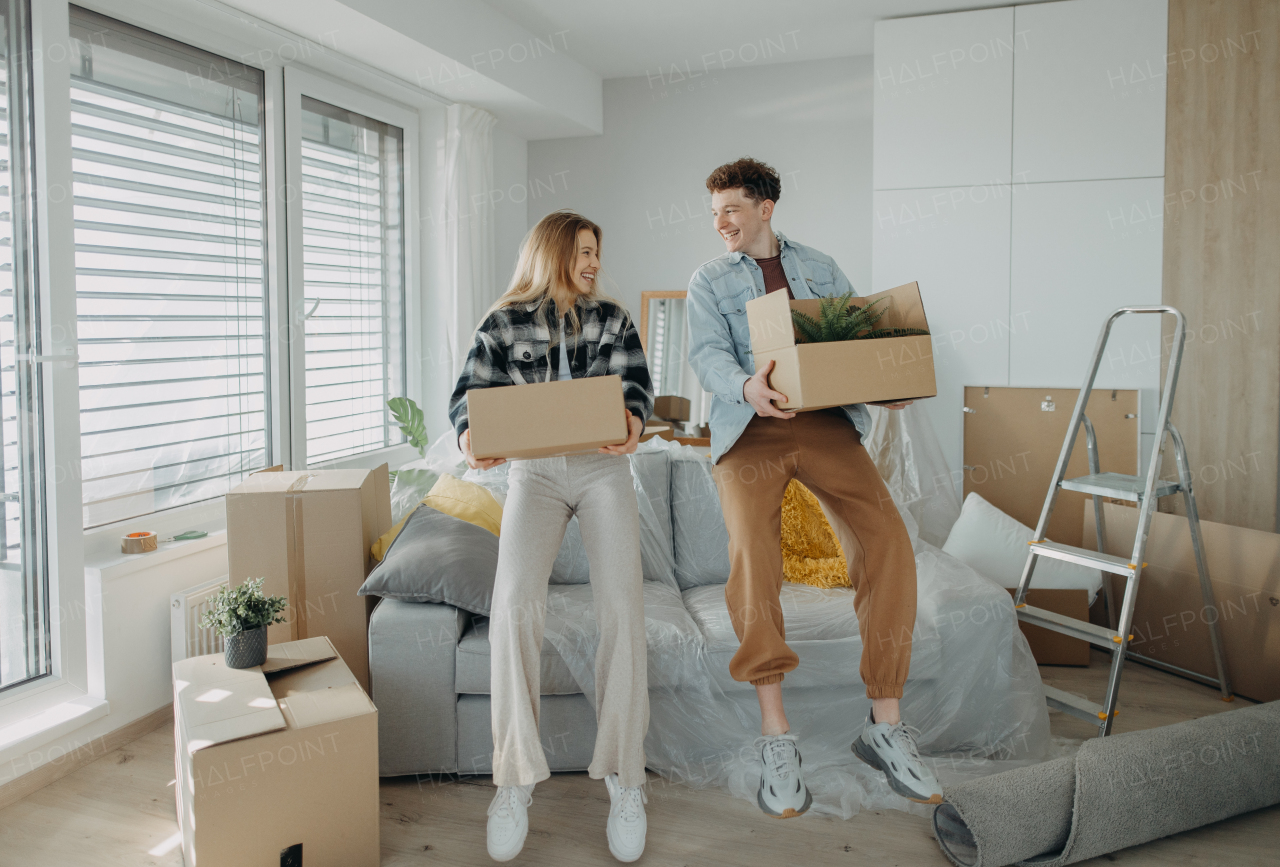 A cheerful young couple in their new apartment, carrying boxes. Conception of moving.