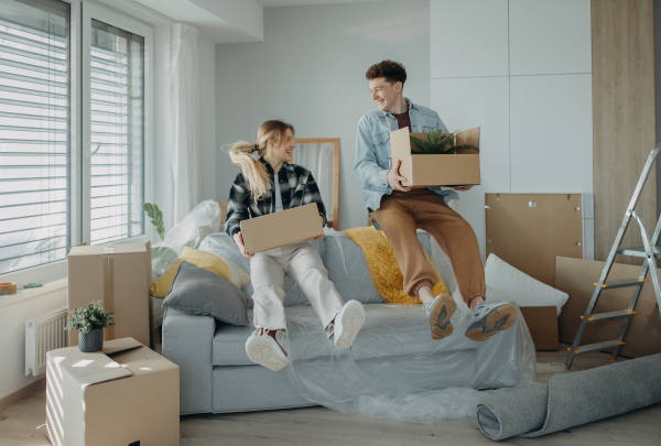 A cheerful young couple in their new apartment, carrying boxes. Conception of moving.