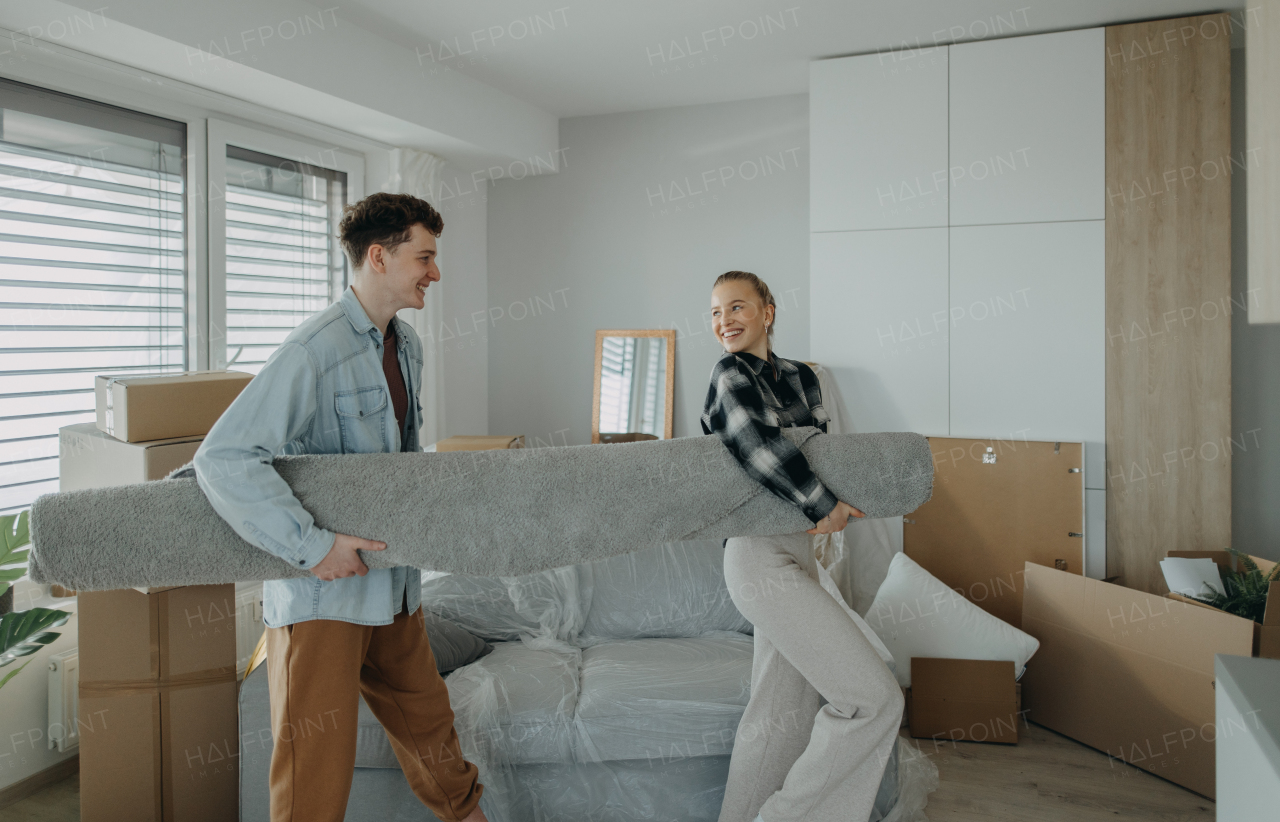 A cheerful young couple in their new apartment, carrying carpet. Conception of moving.