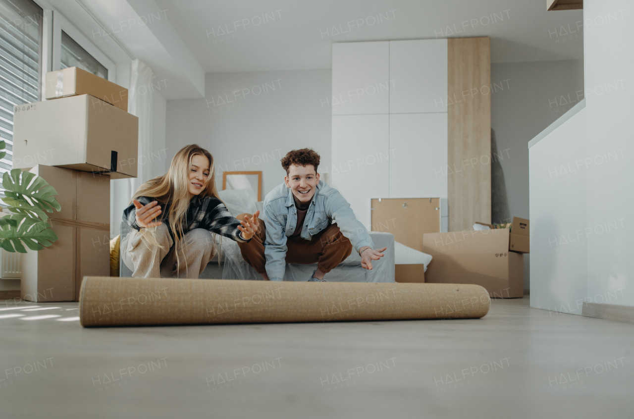 A cheerful young couple in their new apartment, rolling out carpet. Conception of moving.