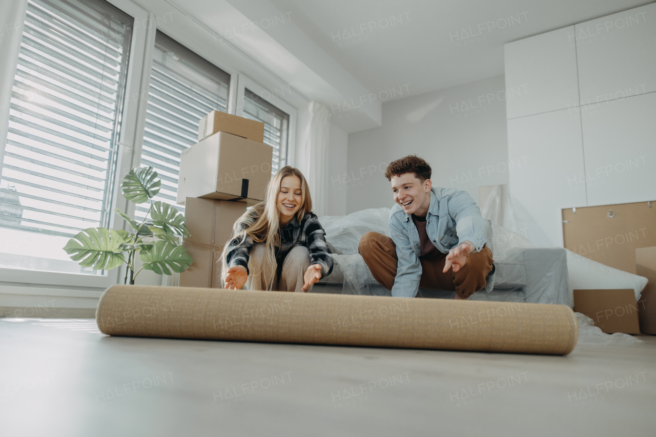 A cheerful young couple in their new apartment, rolling out carpet. Conception of moving.