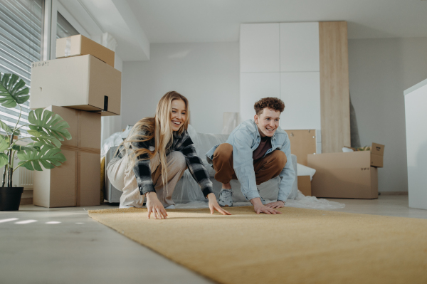 A cheerful young couple in their new apartment, rolling out carpet. Conception of moving.