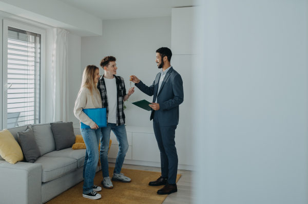 A happy young couple buying their new home and receiving keys from real estate agent