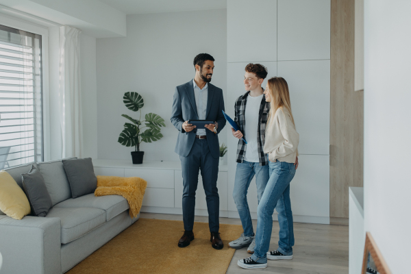 A happy young couple buying their new home and meeting real estate agent in apartment.