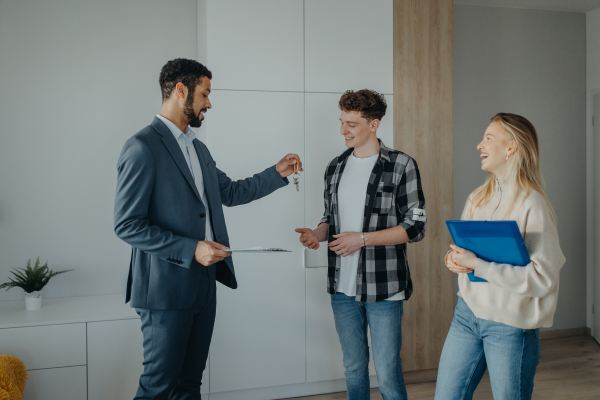 A happy young couple buying their new home and receiving keys from real estate agent