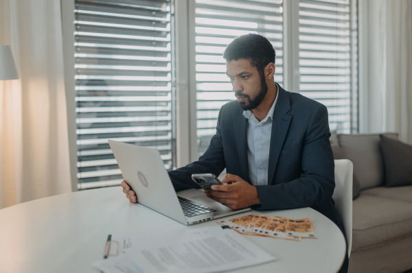 A depressed businessman man counting euro money working on computer at office desk, inflation concept.