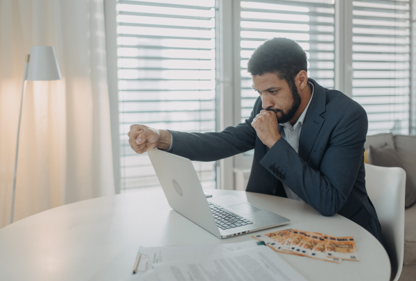 A depressed businessman man counting euro money working on computer at office desk, inflation concept.