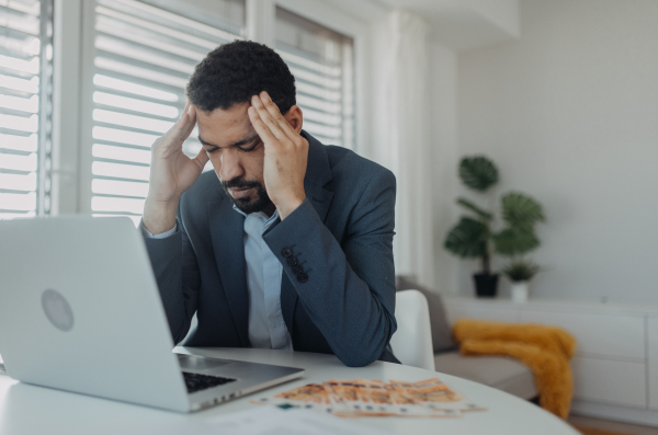 A depressed businessman man counting euro money working on computer at office desk, inflation concept.