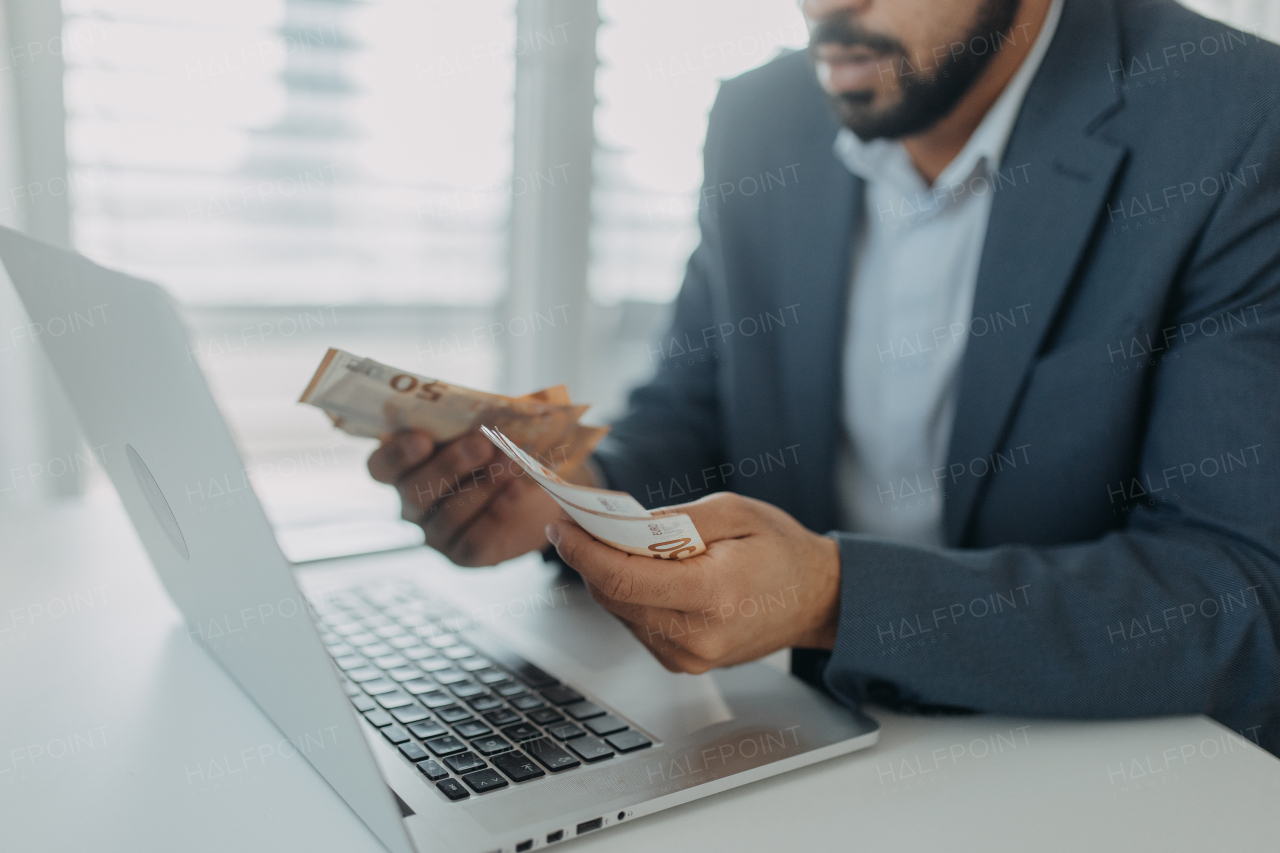 A businessman man with euro money in his hands is working on a computer keyboard at office desk, close-up