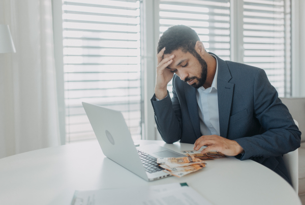 A depressed businessman man counting euro money working on computer at office desk, inflation concept.