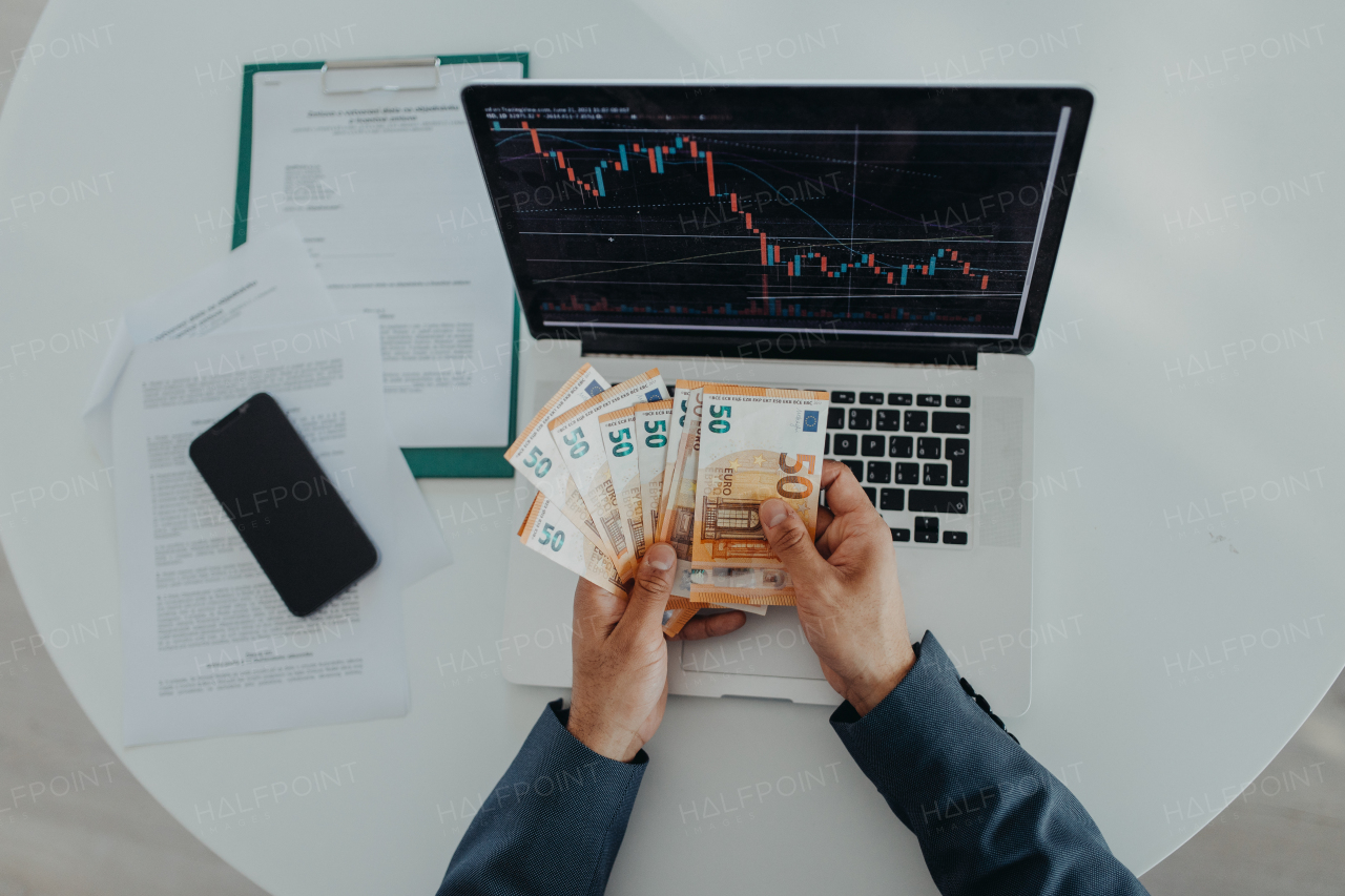 A businessman man counting euro money working on computer at office desk, inflation concept.