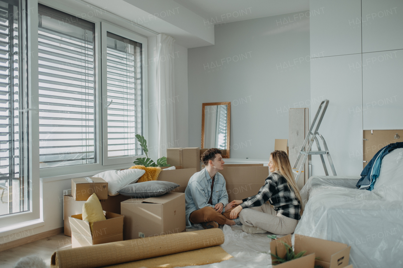 A cheerful young couple in their new apartment, sitting on floor and hugging. Conception of moving.