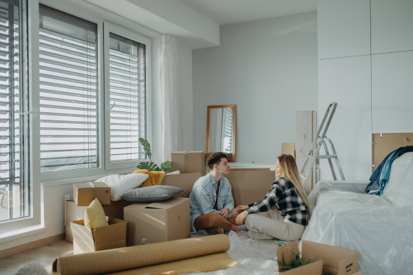 A cheerful young couple in their new apartment, sitting on floor and hugging. Conception of moving.