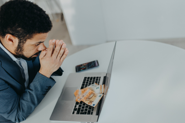 A depressed businessman man counting euro money working on computer at office desk, inflation concept.