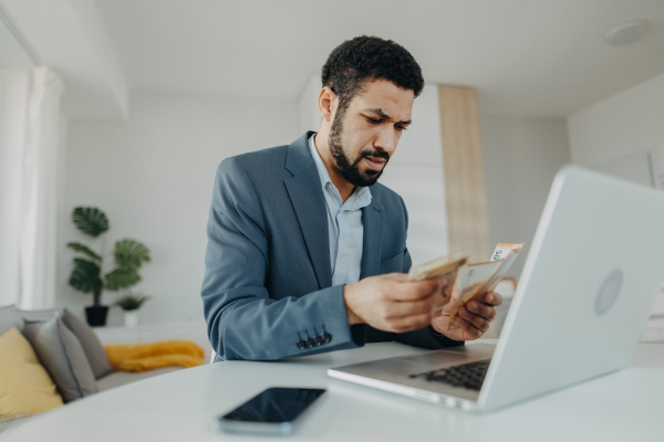 A depressed businessman man counting euro money working on computer at office desk, inflation concept.