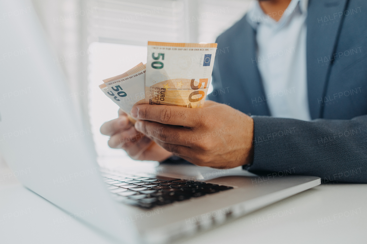 A businessman man with euro money in his hands is working on a computer keyboard at office desk, close-up