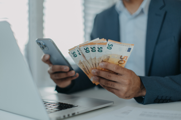 A businessman man with euro money in his hands is working on a computer keyboard at office desk, close-up