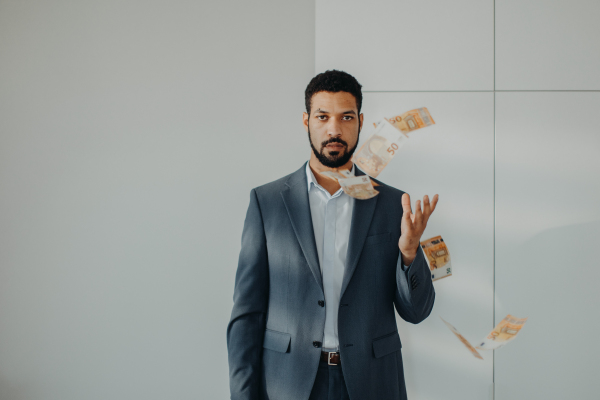 A serious young businessman man standing in officethrowing money away, inflation concept.