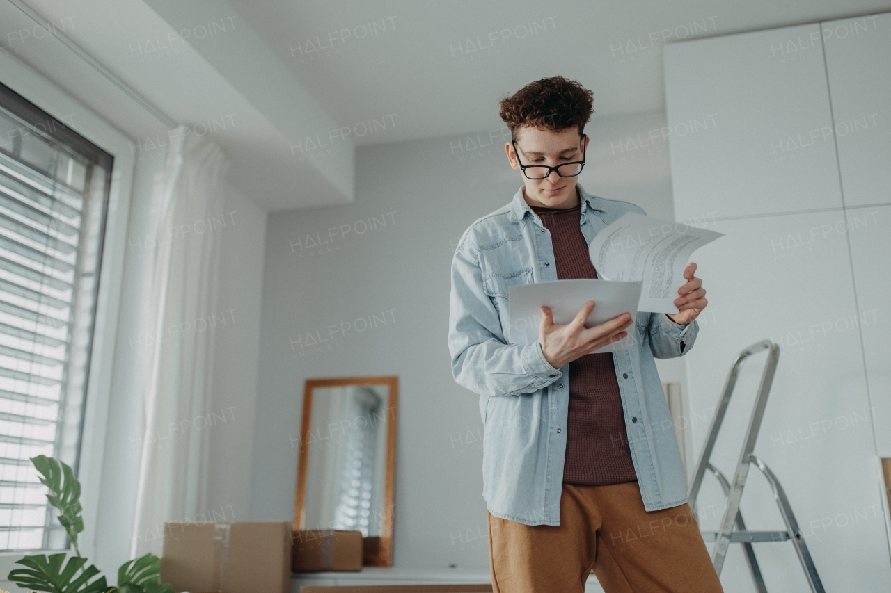 A young man in his new apartment reading contract. Conception of moving.