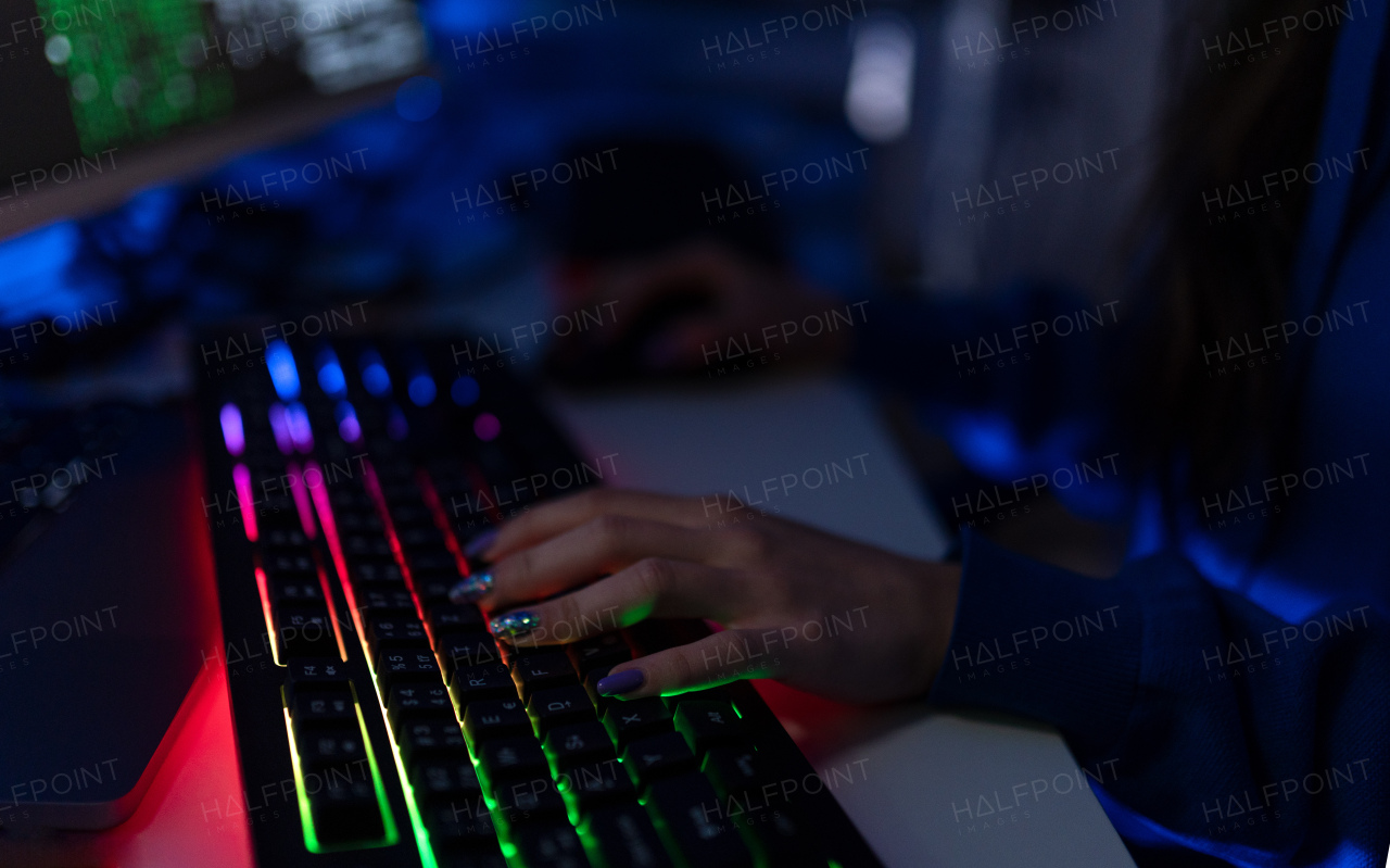 Close-up of a woman hacker hands at keyboard computer in the dark room at night, cyberwar concept. Side view.