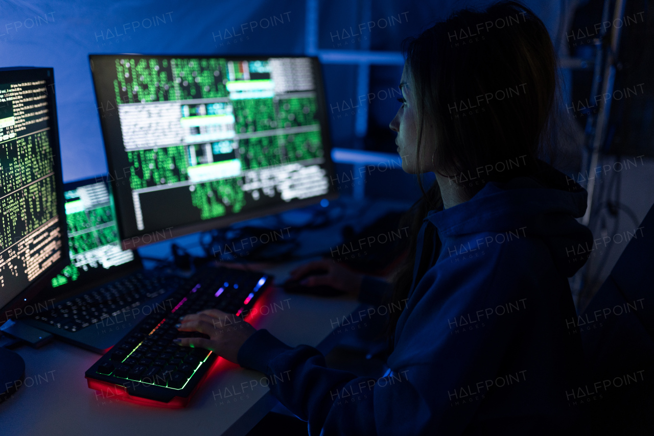 A young woman hacker by computer in the dark room at night, cyberwar concept.