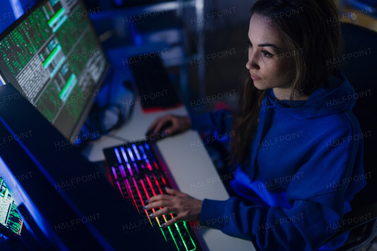 A young woman hacker by computer in the dark room at night, cyberwar concept.