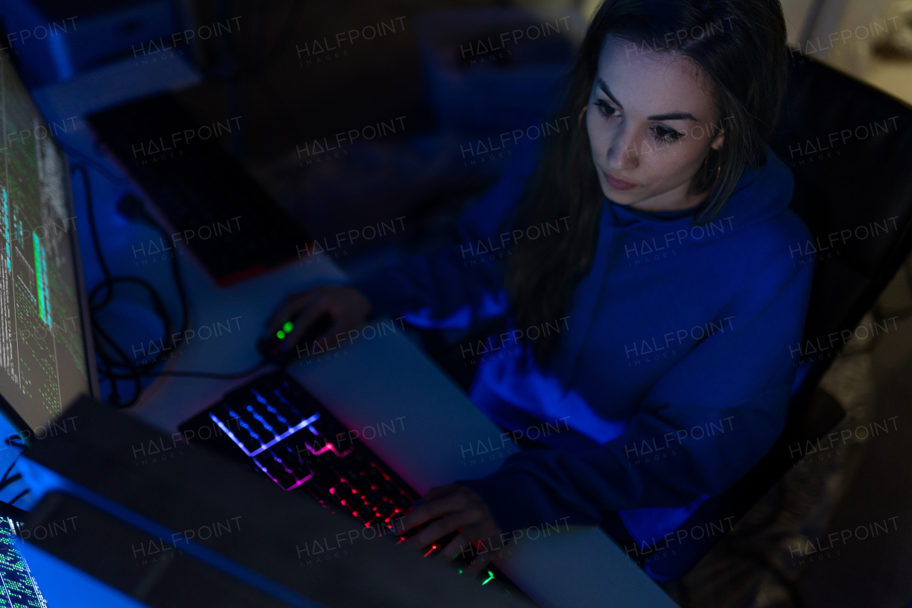 A young woman hacker by computer in the dark room at night, cyberwar concept.