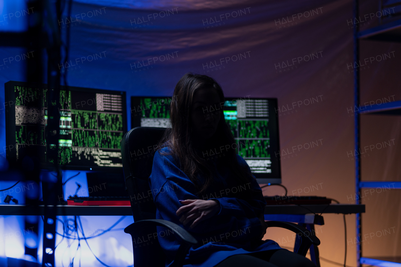 A hooded anonymous hacker woman by computer in the dark room at night, cyberwar concept.