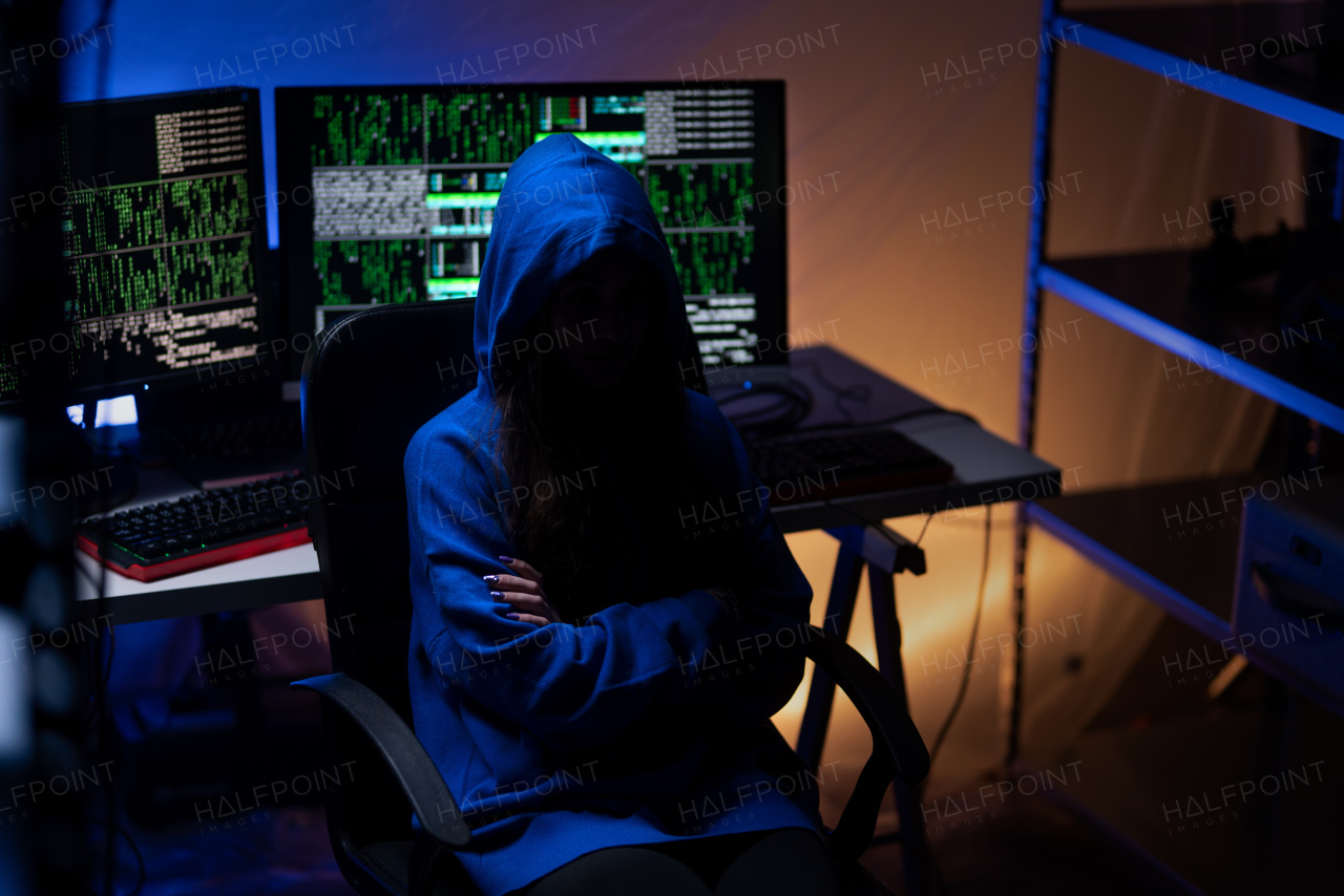 A hooded anonymous hacker by computer in the dark room at night, cyberwar concept.