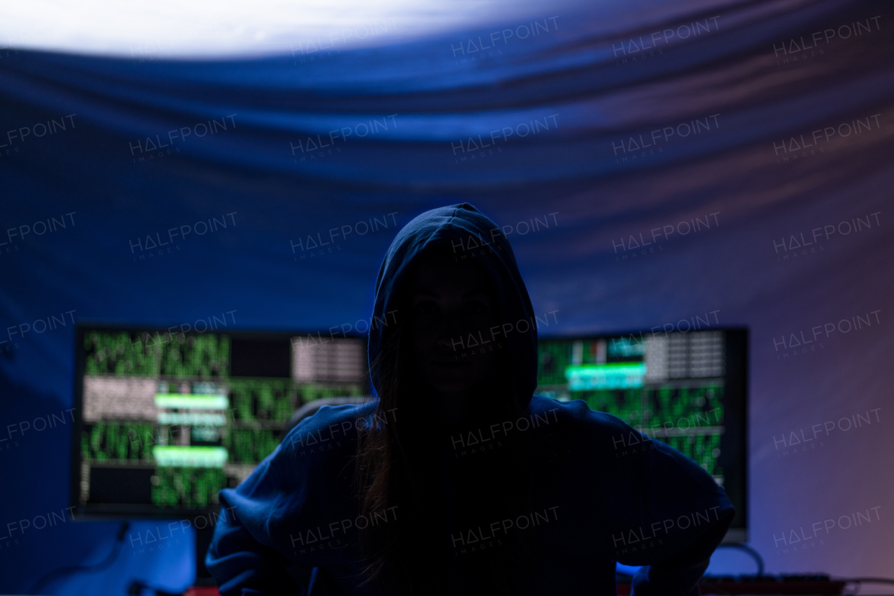 A hooded anonymous hacker by computer in the dark room at night, cyberwar concept.